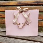 one pink custom solid color gift paper bag with ribbon bow on a wooden bench